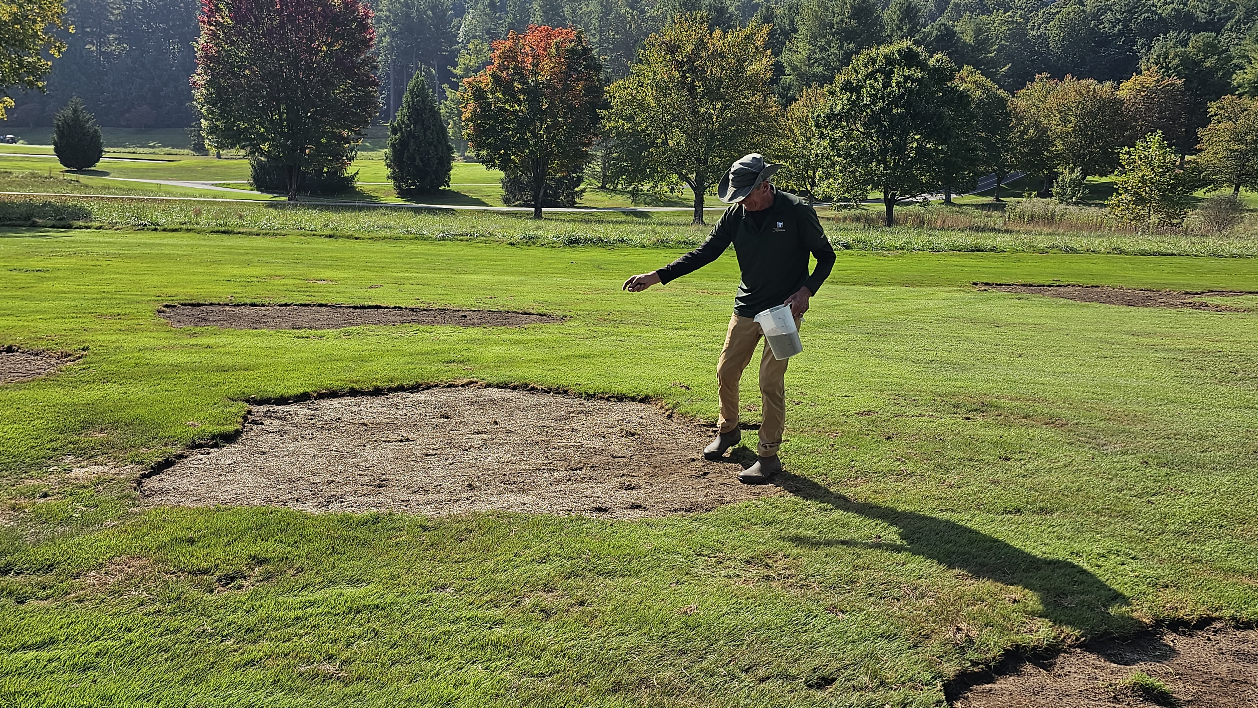 Brad hand broadcasting seed over a fairway repair area